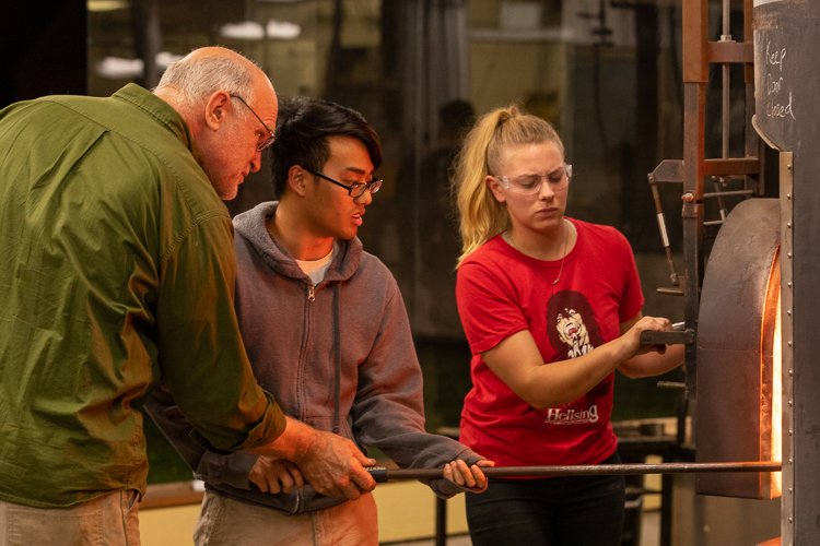 Students working with instructor at glassblowing furnace